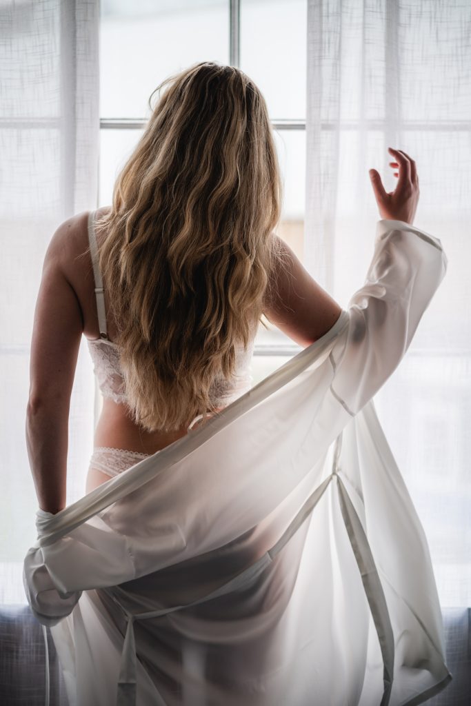 vrouw staat in haar bruidsondergoed met gezicht naar het raam
